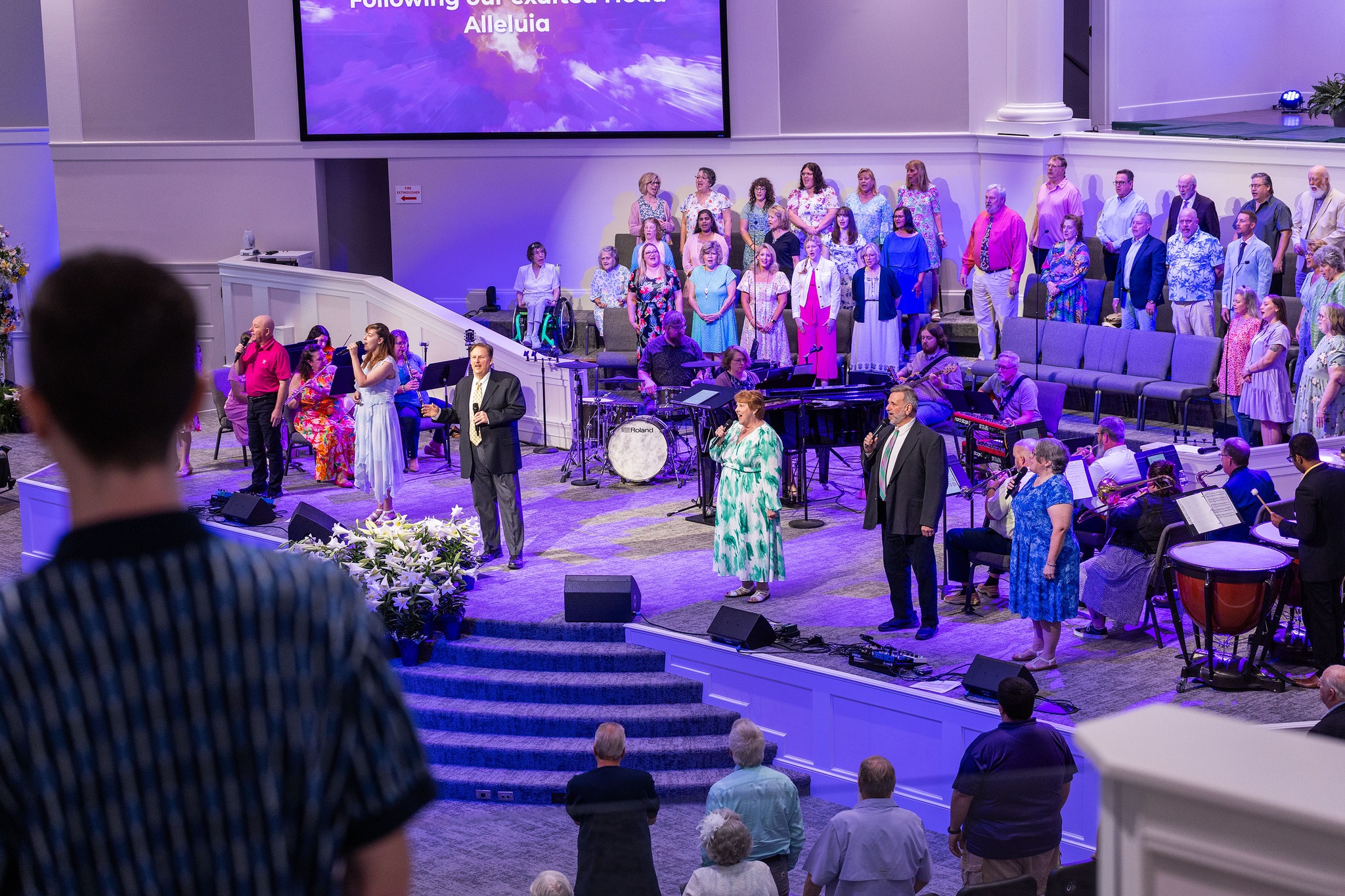 Trinity Baptist Church choir and full worship band performing on stage before a large congregation during a Sunday worship service